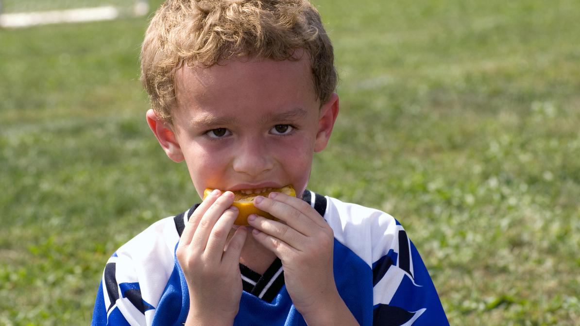 Soccer player eating orange fruit at halftime with red face