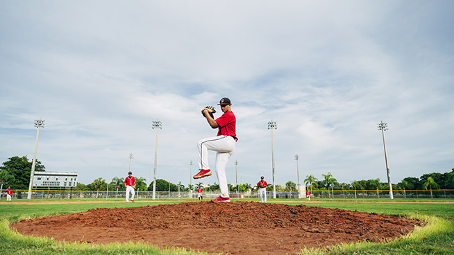 Low angle view of Hispanic baseball pitcher standing on the mound in wind-up position preparing to throw the ball.