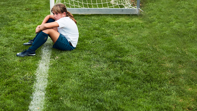 Lifestyle children training and playing soccer. Young girl sitting on the grass after a match defeat.