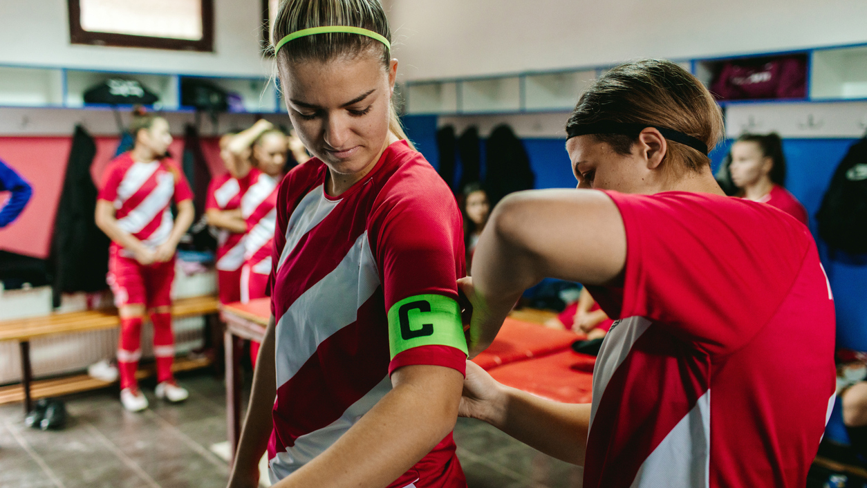 Female soccer player adjusting "captain" arm band to her teammate.