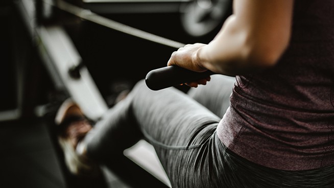 Close up of unrecognizable female athlete having sports training on rowing machine in a gym.