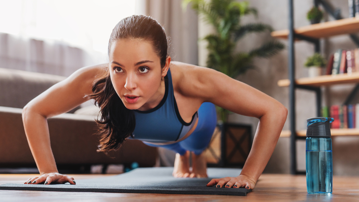 Beautiful young sports lady doing push ups while workout at home