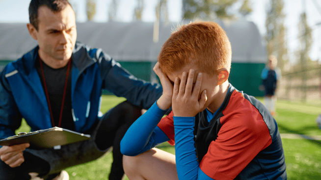 young male soccer player upset and being consoled by coach