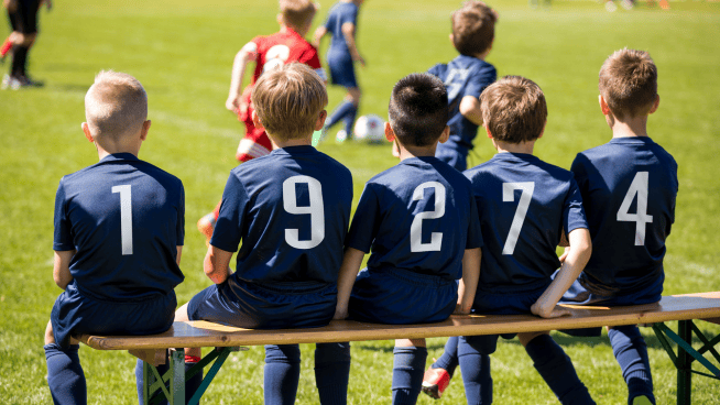young male soccer athletes sitting on bench during a game