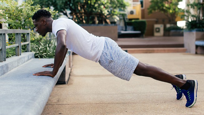 Young African American man doing push up in city park. Male sporty person exercising outdoors