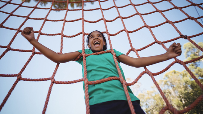 Happy girl cheering while climbing a net during obstacle course in boot camp