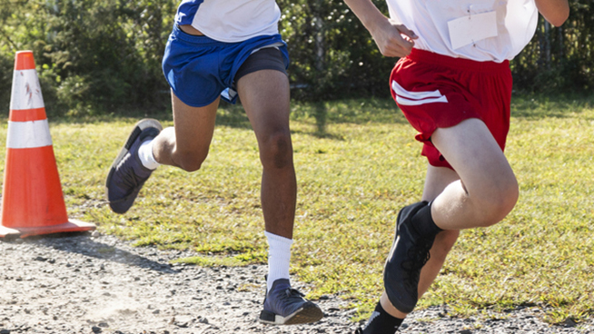 Three high school boys racing on gravel during a cross country race close to the finish.