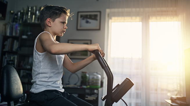 During the COVID-19 pandemic kids are training at home. Little boy is working out on exercise bike at home. Nikon D850