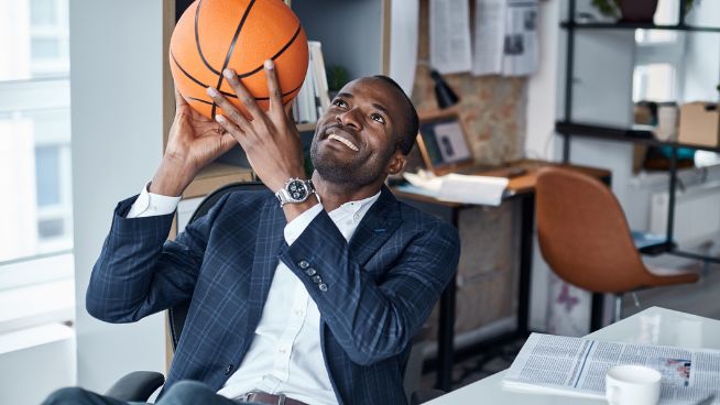 Male sitting at desk in office shooting basketball