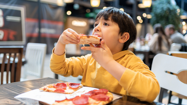 young boy eating pizza at the mall - causes of childhood obesity