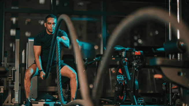 athletic male doing battle rope workout in gym as example of HIIT training to lose fat