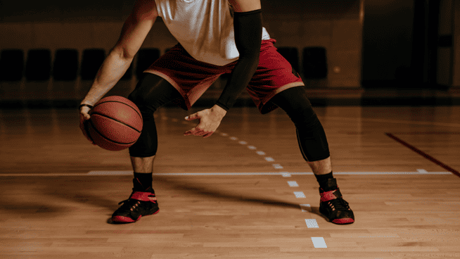 image of male basketball player from the neck down dribbling ball on basketball court - basketball training tips