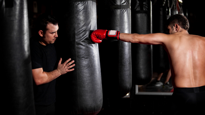 athletic male training for boxing in the gym with trainer - practicing his jab