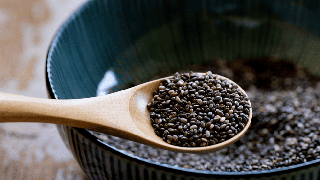 large bowl of chia seeds and wooden spoon full of chia seeds from it - chia seed health benefits - are chia seeds healthy?