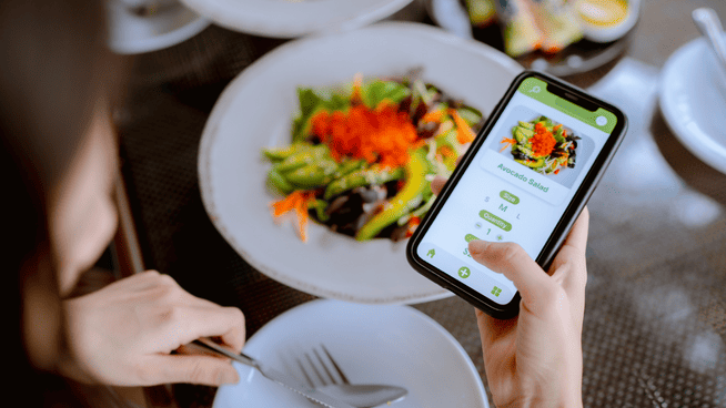 woman at dinner table with salad and phone out to count calories vs macros