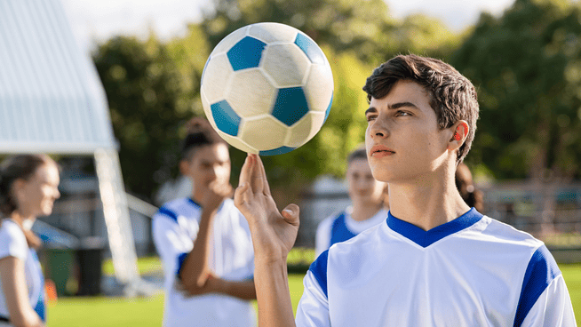 young male soccer player spinning soccer ball on finger - covid recovery for soccer players