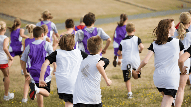 youth cross country teams running together in field - training for cross country running
