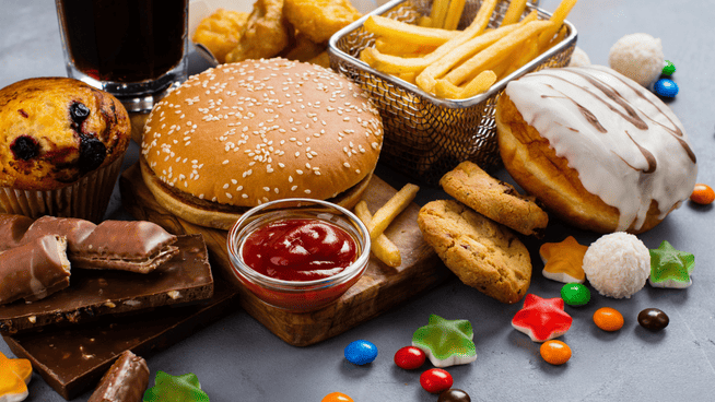 a large selection of fatty foods and sugary snacks on table - is fat or sugar better?