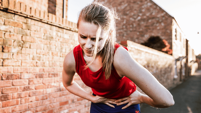 athletic woman bent over in pain grabbing stomach outside on jog or walk - fructose intolerance pain