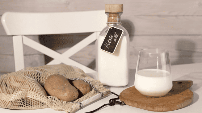 potato milk on table with glass of milk and bag of potatoes