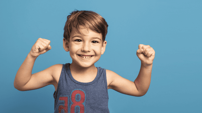young male pre-schooler smiling and flexing his muscles with blue backdrop - strength training for pre-schoolers
