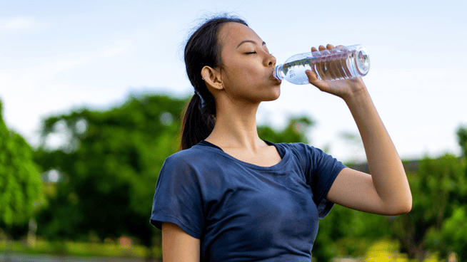 young woman drinking bottled water after run or workout outside - keys to sports recovery for athletes