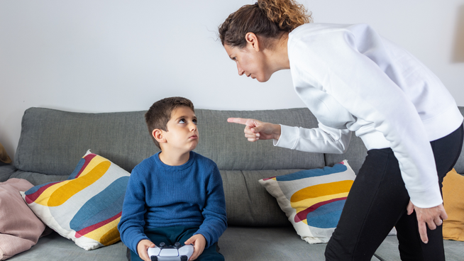 mother disciplining young son sitting on couch playing video games too long