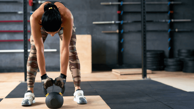 athletic woman bending over doing kettlebell exercise at gym