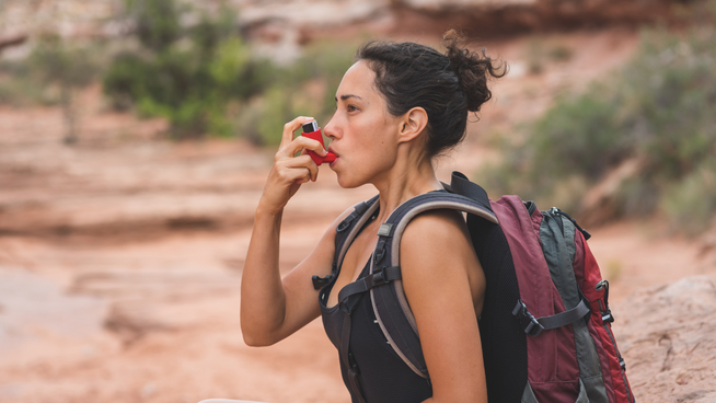 athletic woman with asthma on hiking trip puffing on an inhaler