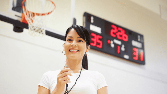 female basketball coach standing in front of basketball goal and scoreboard