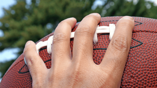 close up image of male hand gripping a football on the laces