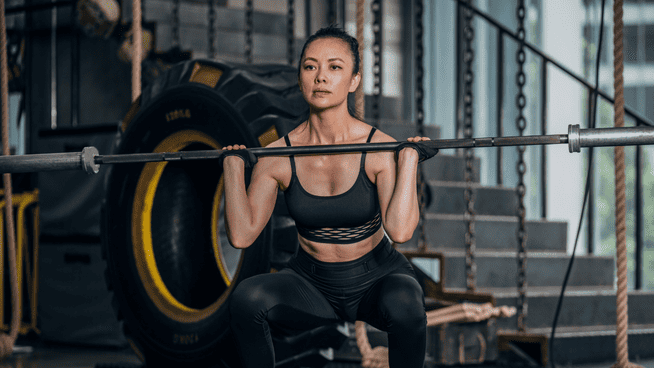 woman performing squat with weight bar at gym