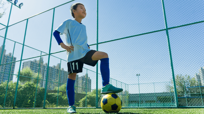 young male soccer player posing for picture with foot on soccer ball at outdoor field in the city