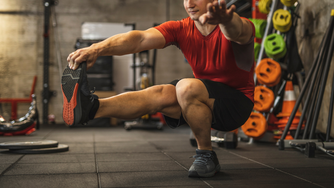 athletic male performing a single leg squat during unilateral training session at the gym