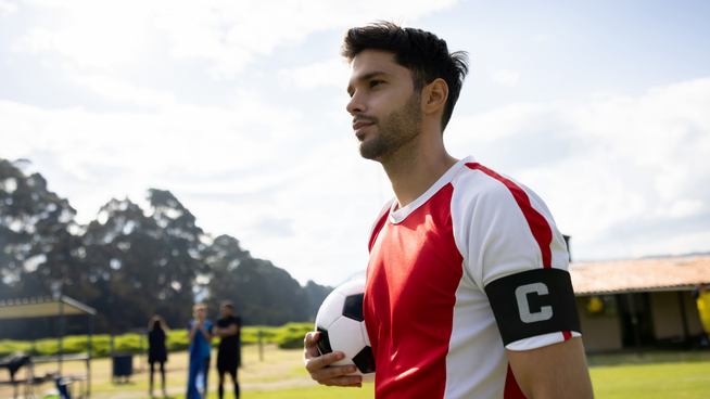 male soccer player team captain holding soccer ball on field