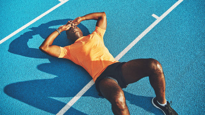 exhausted male athlete laying on track with hands on head for recovery and rest