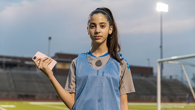youth female athlete holding cell phone in practice soccer jersey on a soccer field
