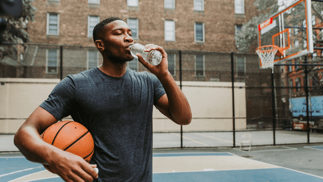 basketball athlete hydrating by drinking water on outside basketball court