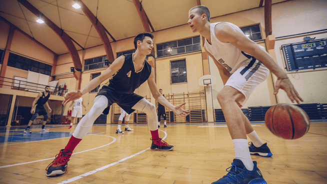 basketball athlete dribbling between his legs against a defensive player in a basketball game