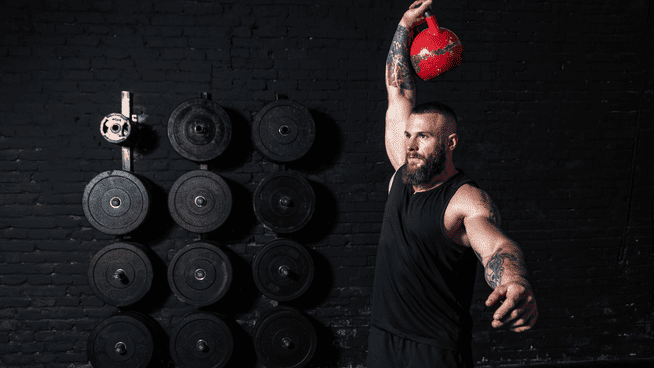 athletic male performing a kettlebell snatch exercise at the gym