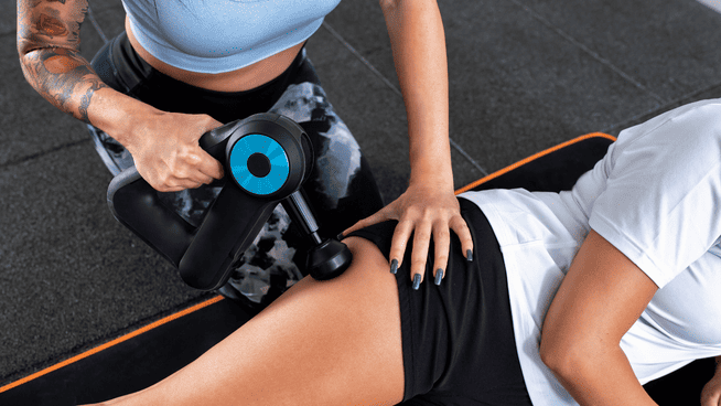 personal trainer using percussion massage gun on athlete experiencing soreness