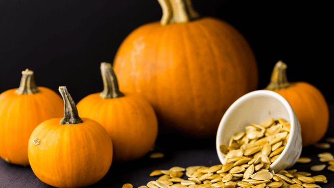 a batch of pumpkins with a bowl of pumpkin seeds spilling out