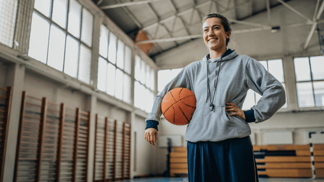 womans college basketball coach holding basketball and smiling in gym