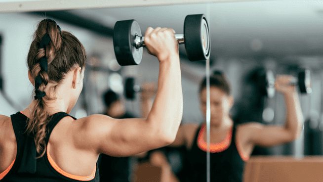 woman performing shoulder exercises with dumbbells at the gym