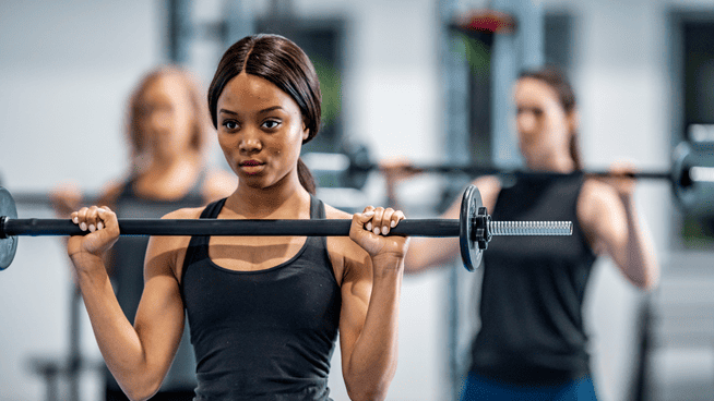 young female working out with barbell in the weight room with others