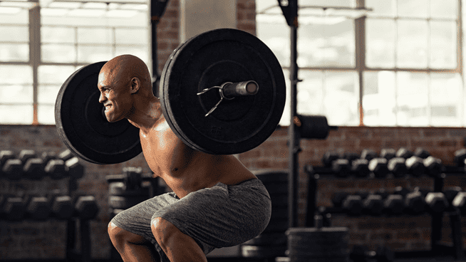 athletic male performing squat exercise at gym