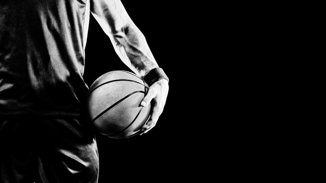 black and white image of basketball players body holding basketball with black background