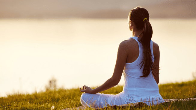 young woman meditating on hill outside overlooking a lake