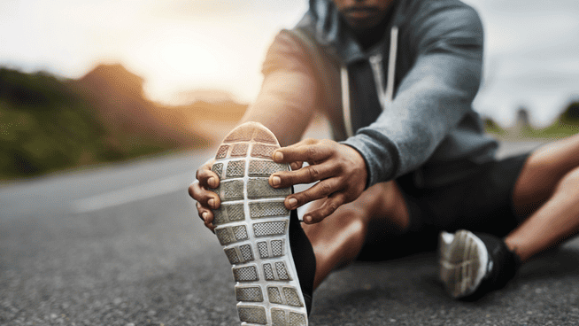 athletic male stretching his hamstring outside before a jog