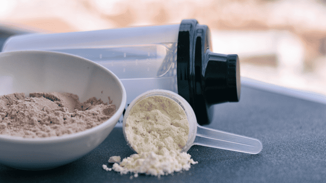 whey protein powder with shaker and scooper on table